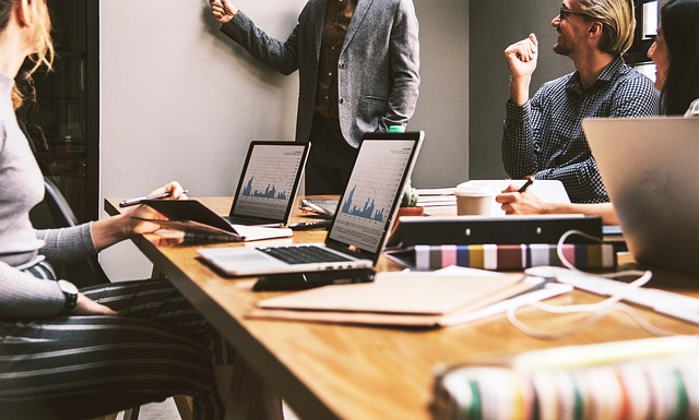 A business team collaboratively analyzing charts and graphs displayed on laptops during a meeting in a modern office setting.