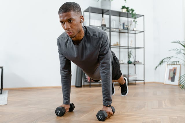 A man performing push-ups at home, holding dumbbells for added resistance, illustrating effective home workout plans for strength and fitness.