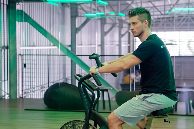 A focused man is shown using an air bike in a modern gym setting. This image can illustrate the importance of incorporating cardiovascular exercise for endurance within a 'Muscle Building at Home Workout Plan'. It emphasizes how cardio supports muscle growth by improving overall fitness and recovery.