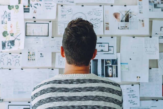 A man from behind looks at a wall covered in notes, sketches, and images, representing planning and strategy for achieving goals at home.